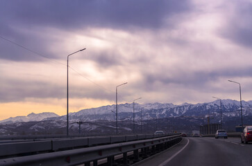 a highway with cars, a gloomy sky over mountains and cities