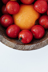 red and yellow tomatoes covered with water drops in a wooden bowl on a white background