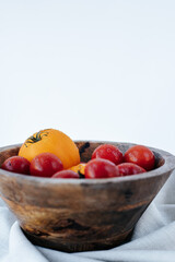 red and yellow tomatoes covered with water drops in a wooden bowl on a white background