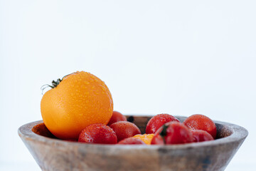 red and yellow tomatoes covered with water drops in a wooden bowl on a white background