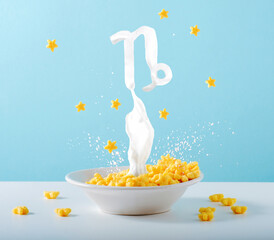 Zodiac sign Capricorn made of milk levitates over breakfast plate of cornflakes and milk on blue background. Creative astrological postcard.