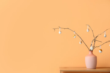 Vase with tree branches and Easter eggs on shelf near beige wall