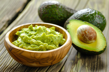 Halved avocado and guacamole in wooden bowl for healthy food concepts. - obrazy, fototapety, plakaty