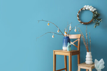 Vase with tree branches and Easter eggs on chair near blue wall in room