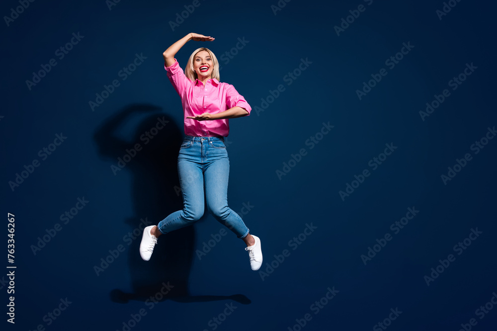 Wall mural Full body photo of attractive young woman jumping show measure gesture wear trendy pink clothes isolated on dark blue color background