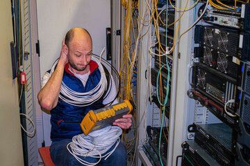 A technician, entangled in wires, measures the signal level in the server room. A man scratches his head wondering how to fix the connection in a data center.