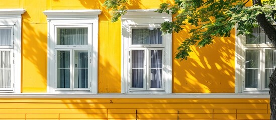 Fototapeta premium Against the backdrop of a sunny spring day, a yellow building adorned with three windows and white trim gleams with vitality. Its radiant hue exudes joy and optimism