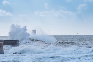 Storm waves over lighthouse, Portugal - sky enhanced. Windy coast. Bad weather with waves crashing in Porto harbor.