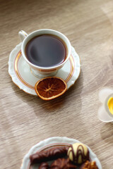 Easter eggs in the basket, bowl of cookies, chocolate pralines, Easter bunny figurine, cups of tea, glasses of juice, flowers and lit candles on the table. Selective focus.