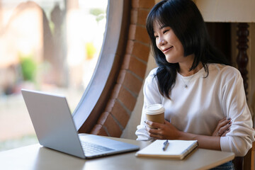 Young Asian woman taking a coffee break while working remotely in a coffee shop.
