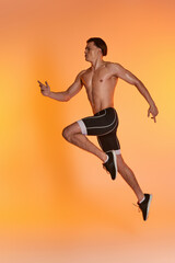 Fototapeta na wymiar appealing shirtless man in black shorts exercising actively and looking away on orange backdrop