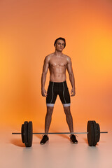 Fototapeta na wymiar alluring shirtless young man in black sport shorts exercising with barbell and looking at camera