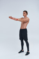 alluring athletic young man in black pants posing topless with resistance band and looking away