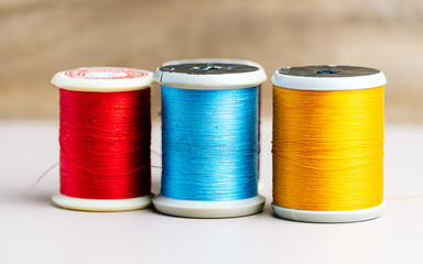 Three spools of thread in vibrant red, blue, and yellow stand in a row against a neutral background, illustrating the basic tools of sewing and textile arts.