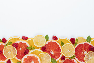 slices of orange, lemon and grapefruit, mint leaves and raspberries are laid out on one side of the frame on a white background
