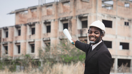 African engineer manager holding and checking blueprint for demolition construction plan and rebuild at the site