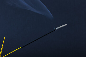 A closeup of incense stick and wavy shaped fume on the black textured background for graphic and...