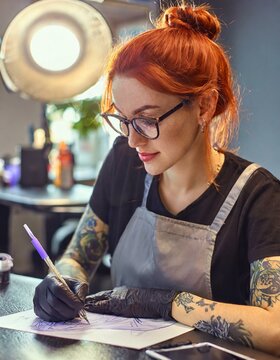  Woman master in a tattoo parlor makes a sketch of a future tattoo