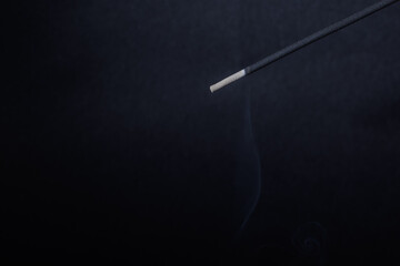 A closeup of incense stick and its fume on the black textured background for graphic and web design use