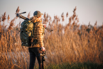 Woman birdwatcher with backpack, tripod and binoculars is doing observation of birds in nature