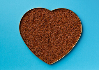 Chocolate chips, sprinkles in a heart-shaped box on a blue background.