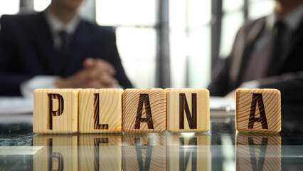 Businessmen in the office are talking in close-up, with the word PLAN in the foreground