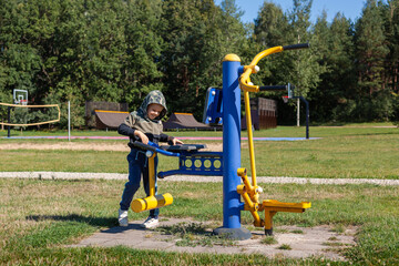 A little boy in a hooded sweatshirt familiarizes himself with a training device on an outdoor...