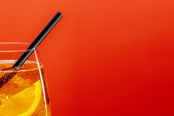 Detail of aperol spritz aperitif with orange slice, ice cubes and black drinking straw on bright...
