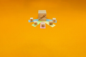鉛筆の周りに付せんにのったスタディの英語ブロックが広がるオレンジ色の背景 - obrazy, fototapety, plakaty