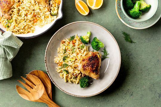 Bowl with chicken, pasta orzo with vegetables in Mediterranean style on a green background.
