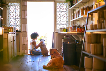 Woman With Pet Dogs Sitting In Doorway Of Sustainable Plastic Free Grocery Store