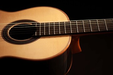 Fototapeta premium Classical Spanish flamenco guitar close up, dramatically lit isolated on black background with copy space.