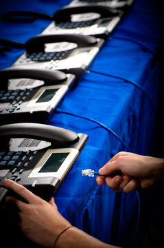 A hand plugs a phone cable into a telephone on a table full of phones in a call center