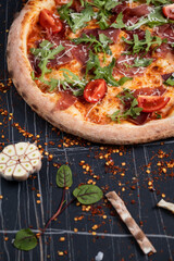 Baked pizza with salami, prosciutto and chicken with red sauce and melted cheese on a black wooden background in a composition with ingredients. Top view