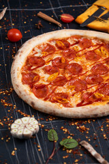 Spicy pizza with sausages and chili peppers. On a black stone background. Free space for text.