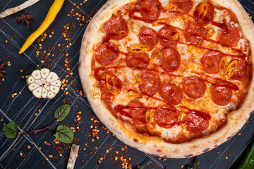 Spicy pizza with sausages and chili peppers. On a black stone background. Free space for text.