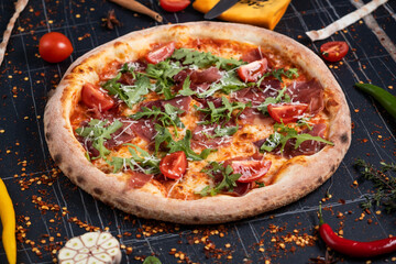 Baked pizza with salami, prosciutto and chicken with red sauce and melted cheese on a black wooden background in a composition with ingredients. Top view