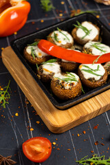 Stuffed portobello mushrooms stuffed with mozzarella and gorgonzola cheese and aromatic herbs on a black background, top view. Vegetarian food
