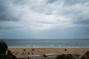 Rainy day on summer holiday vacation looking at sea view through balcony glass window with focus on rain drops. Portimao Algarve Portugal tourist destination bad weather raining and cloudy day 