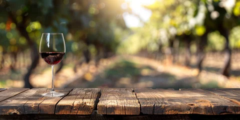 Foto auf Glas Wood table top with a glass of red wine on blurred vineyard landscape background © Ricardo Costa