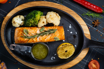Fried salmon steak with spinach, lemon and cherry tomatoes served on black plate on wooden table