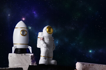 Figurine of astronaut and rocket over sky background, copy space. Toy of spaceman and cosmos...