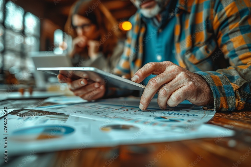Poster an older man with glasses reviews financial charts and data on paper documents using a digital table