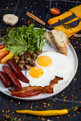English Breakfast in cooking pan with fried eggs, sausages, bacon, beans, toasts and coffee on dark stone background copy space