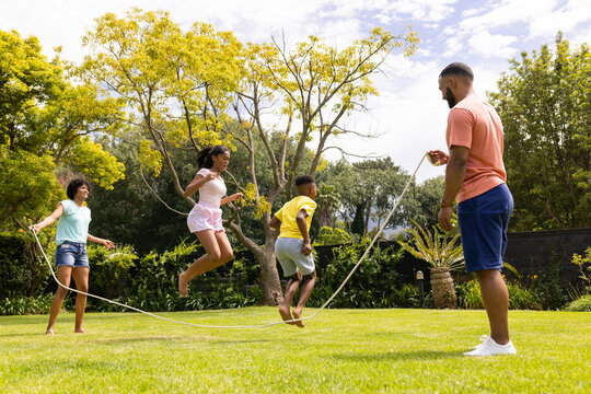 An African American family enjoys jumping rope together in a lush garden