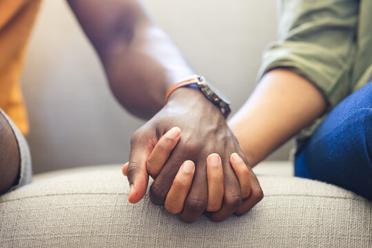A diverse couple holds hands on the couch, showing unity and affection