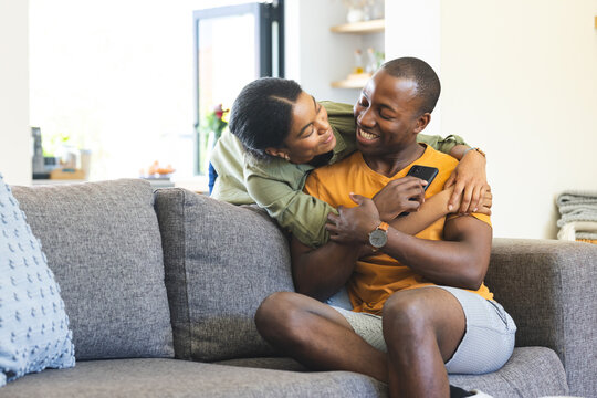 A young African American couple shares a cozy moment on the sofa at home with copy space