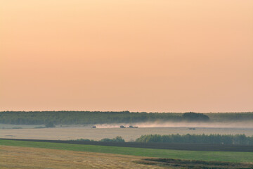 harvesters in in the distant fields in the evening