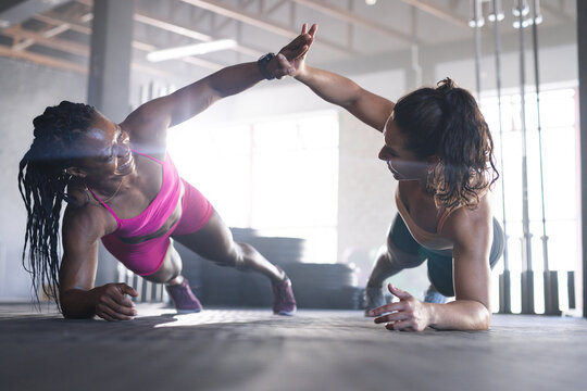 Two fit women are giving high-fives during a workout session in the gym