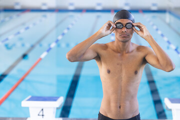 A fit young African American male athlete swimmer adjusts his swimming goggles